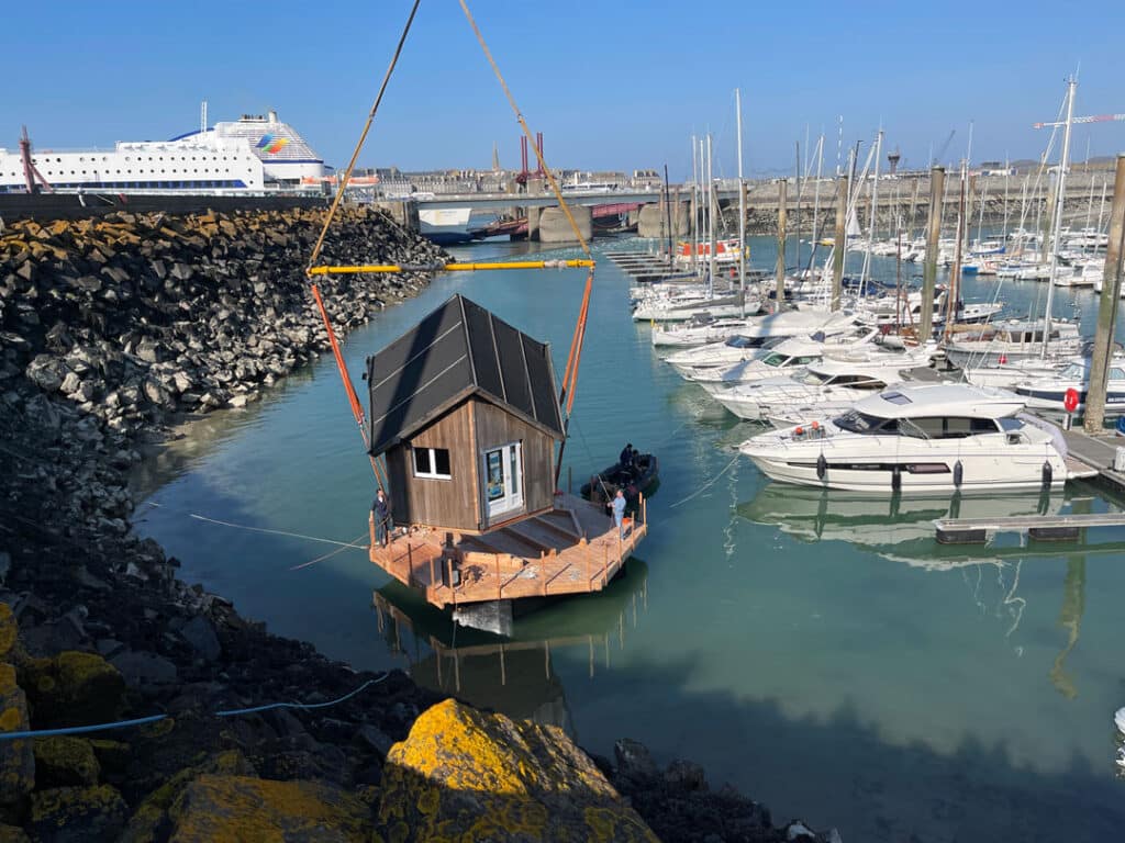 une grue pose la tiny house flottante sur l'eau